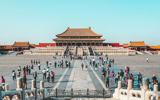 Visitors crossing the great stone courtyard of the Forbidden City in Beijing under a clear sky