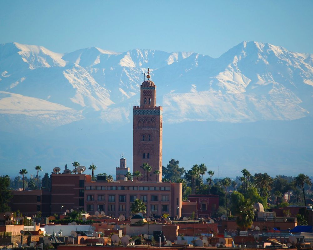 The minaret of the Koutoubia mosque above the rooftops of Marrakech, with the snow-capped Atlas mountains behind