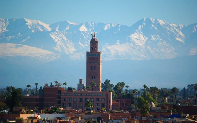 The minaret of the Koutoubia mosque above the rooftops of Marrakech, with the snow-capped Atlas mountains behind