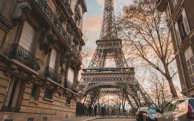 A cobbled Paris street lined with stone apartment buildings, the Eiffel Tower rising at the end