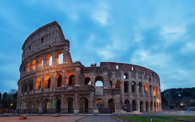 The Colosseum in Rome at dusk, its arches lit warm orange under a blue evening sky